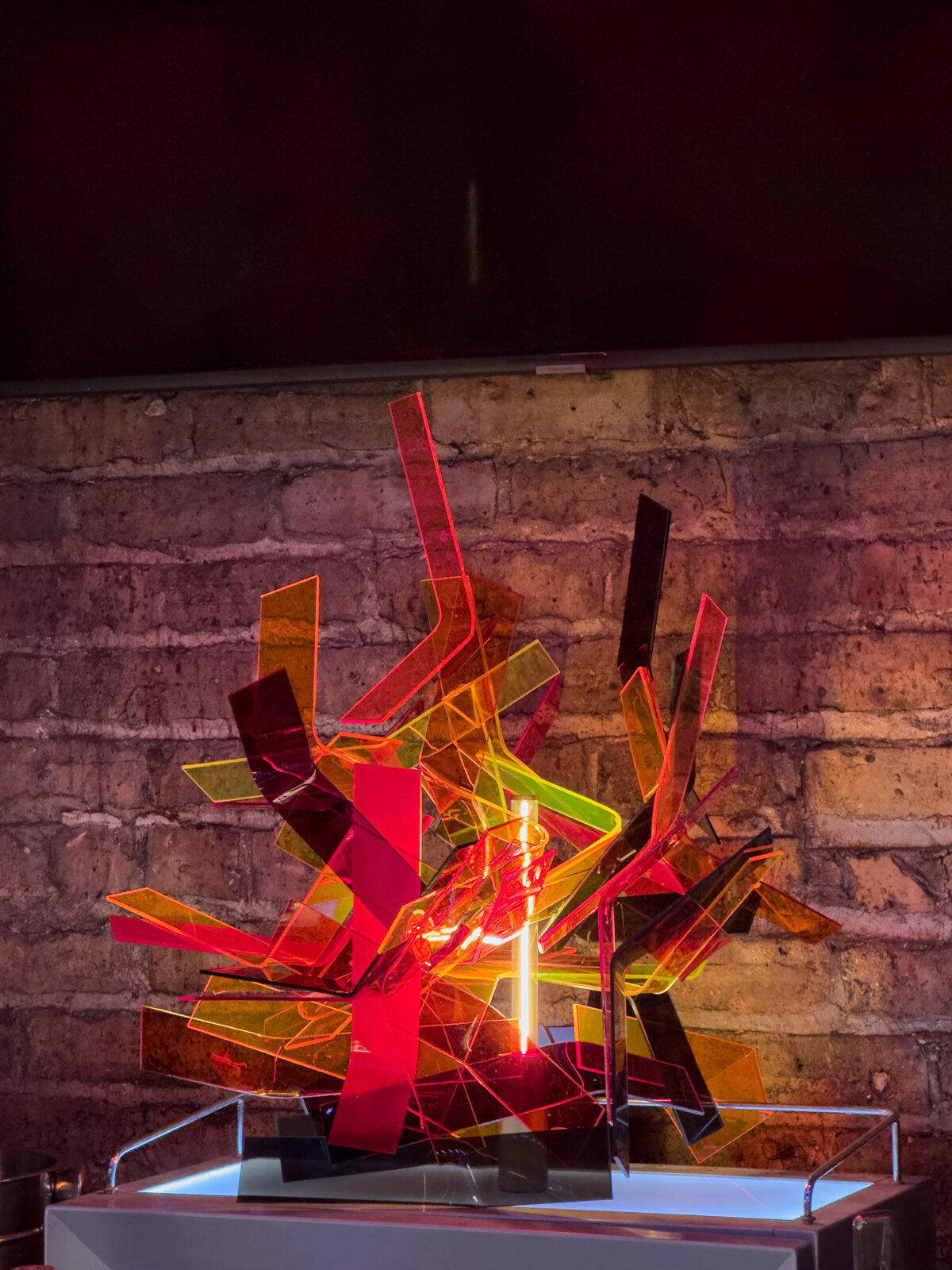 Flame Core, translucent and fluorescent acrylic sculpture with found light, installed against a brick wall